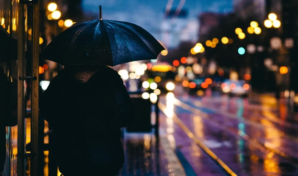 Person mit Regenschirm in einer nassen Straße am Abend